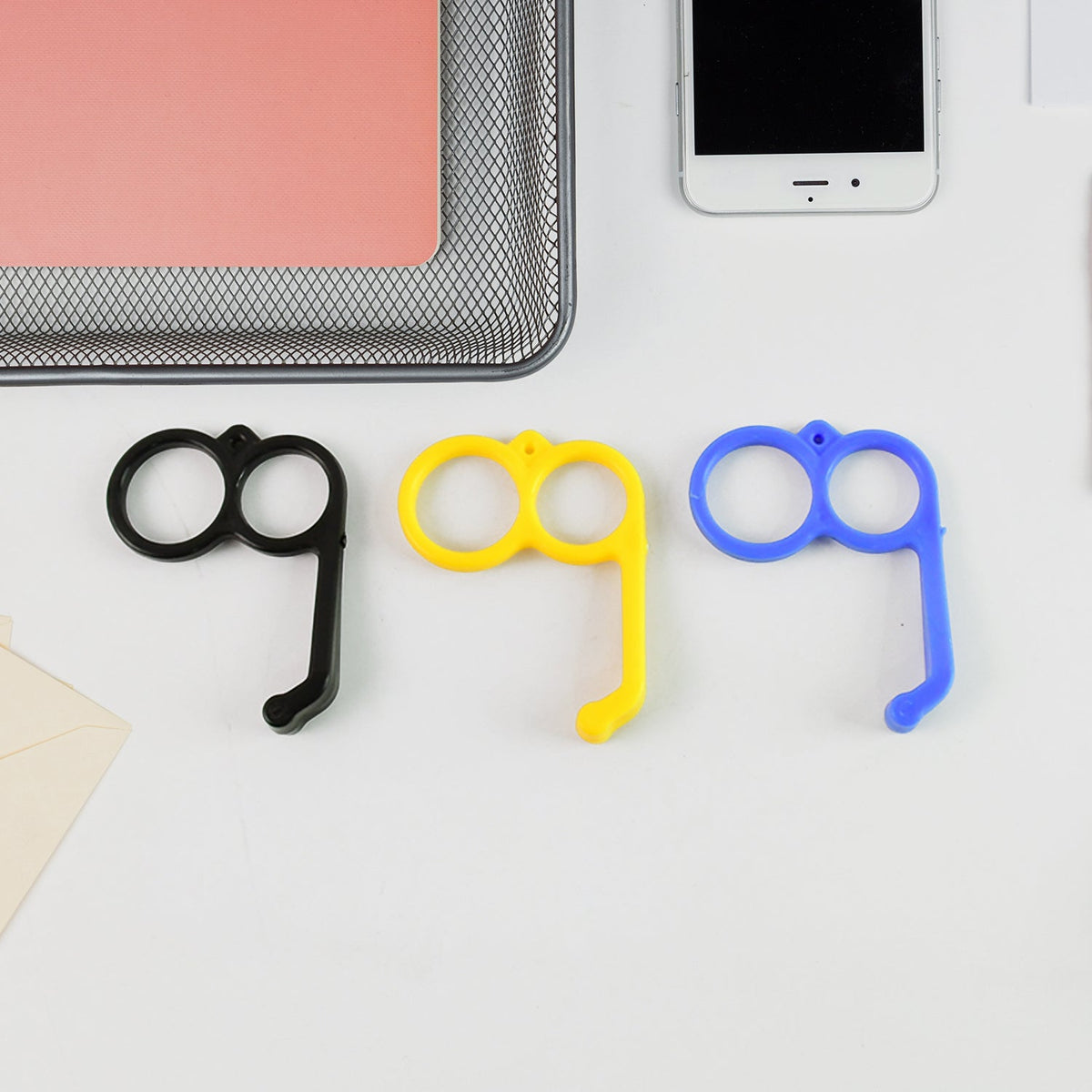 Three plastic finger ring phone holders in black, yellow, and blue on a white desk.