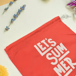 Close-up of a red drawstring bag with "LET'S SUMMER" and Havaianas logo, with purple and yellow flowers in the background.