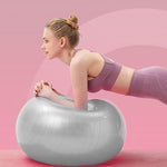 A woman in a purple sports bra and leggings holds a plank position with her forearms on a grey stability ball, against a