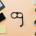 A black plastic finger ring phone holder lies on a peach-colored surface surrounded by electronics.