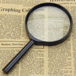 A black magnifying glass lies on an open newspaper, enlarging a section of the text on the page.
