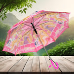 A pink umbrella with princess characters is open on a wooden surface, with a lush green forest and mountains in the