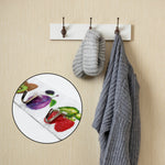 A close-up of the fruit-themed adhesive hooks is inset over a blurred image of a different, plain white coat rack with a hat