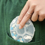 A hand placing a clear 7-day pill organizer with blue and white pills into a green pocket.