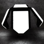 The white and black foldable LED lantern with its panels partially open, glowing brightly in a dark setting.