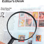 A black magnifying glass magnifies a section of a magazine page featuring various celebrity covers.