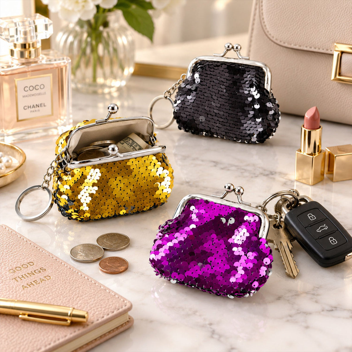Three sequined coin purse keychains in gold, black, and purple on a marble vanity, one holding coins and a key fob.