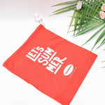 A red drawstring bag with "LET'S SUMMER" and Havaianas logo, angled on a white surface with palm leaves and small pink