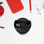 A black power converter plug is centered on a white surface, surrounded by red tech accessories.