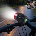 A red and black bicycle headlight with a green button illuminates a dark road from a bike's handlebars.