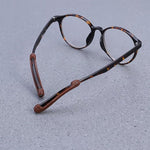 Tortoiseshell eyeglasses with brown anti-slip ear grips on the temples, resting on a gray textured surface.