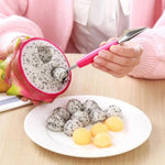 A person uses a pink-handled tool to scoop fruit from a halved dragon fruit, with dragon fruit and melon balls on a white