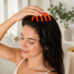 A woman with wet, dark hair gently massages her scalp with an orange, five-pronged plastic tool.