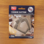 A packaged set of three stainless steel house-shaped cookie cutters on a light brown wooden surface.