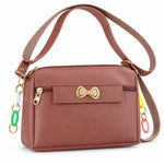 A mauve sling bag with a gold bow and colorful charms on a white background, angled view.