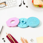 A disassembled blue and pink cookie eraser lays on a white desk with pencils, a sharpener, and other office items.
