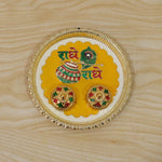 A silver and yellow Radhe Radhe pooja thali set with two small decorative containers on a light wooden background.