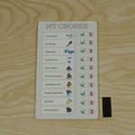 A white chore board with all tasks marked complete, resting on a light wooden surface next to a black rectangular magnet.