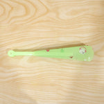 A folded green plastic fan with a bear and apple pattern lies on a light wooden surface.