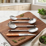 A top-down view of five stainless steel kitchen tools, including a knife with a wooden handle, on a white marble surface.