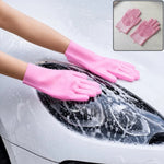 A person wearing pink silicone gloves with scrubbers on the palms and fingers, washing a white car with soap suds.
