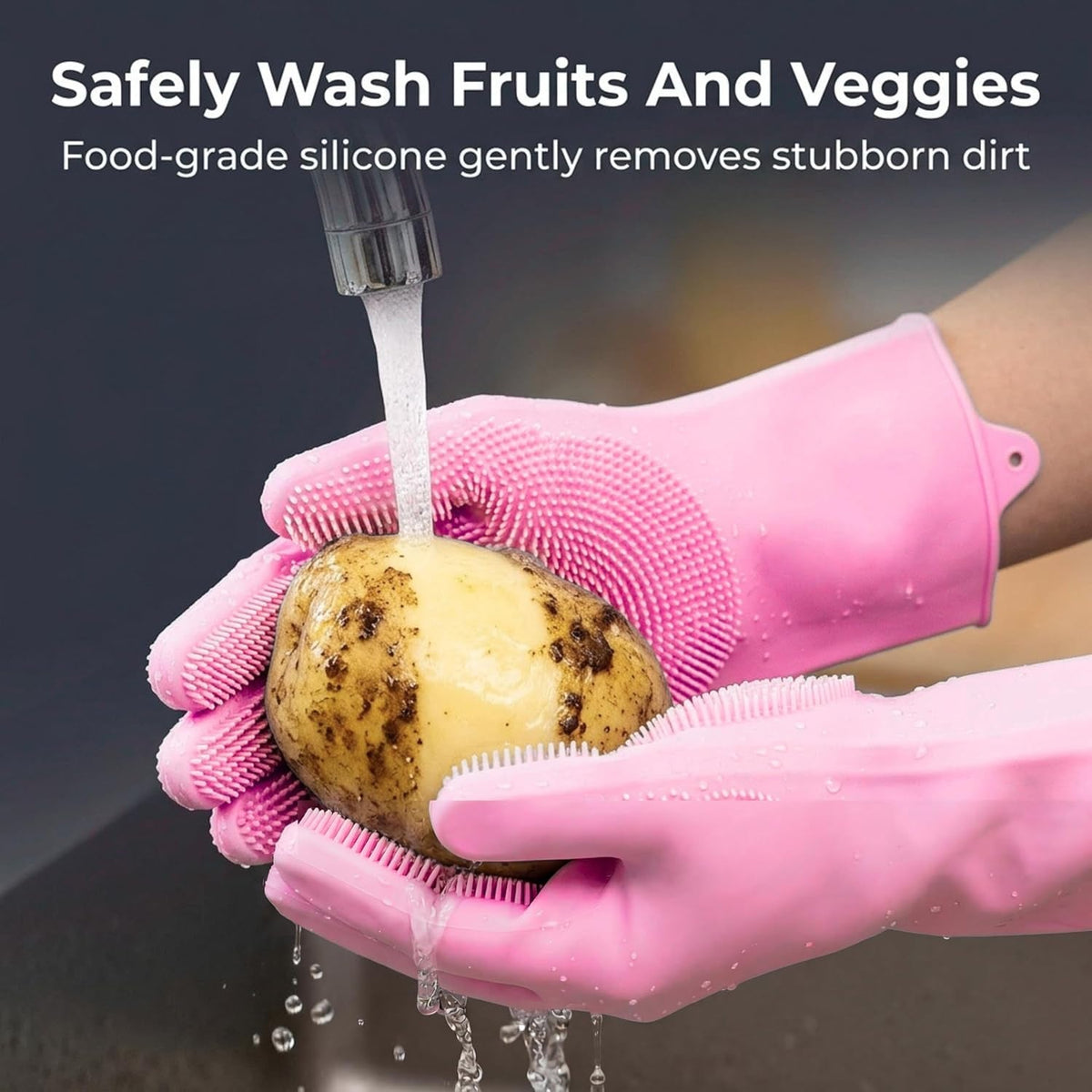 Hands in pink silicone scrubber gloves washing a potato under running water in a kitchen sink.