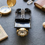 A black and gold headlamp with a solar panel and head strap, surrounded by a compass, rocks, and a notebook on a dark