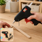 A person's hands using a black and red glue gun to apply hot glue to two pieces of light wood
