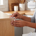A person's hands applying a clear, rounded corner protector to a light wood table edge in a kitchen. – view 7