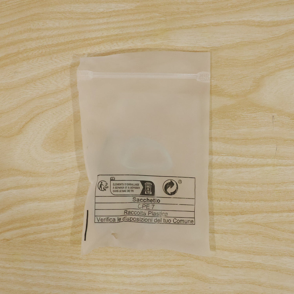 A translucent plastic bag with recycling information printed on it, lying flat on a light wooden surface.
