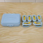 A light blue plastic storage case and six blue and yellow plastic clips are arranged on a light wooden surface.