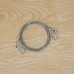A coiled silver wire rope with two attached locking hooks on a light wooden background.