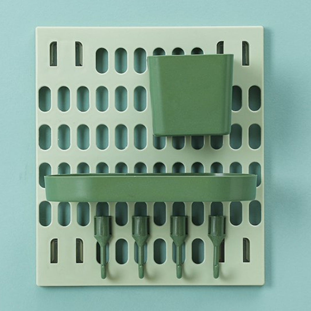 A light green pegboard with a dark green square cup and an oval tray, and four dark green hooks on a light blue background.