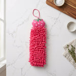 A pink microfiber hand towel with a strawberry top lies flat on a white marble countertop next to a wooden cutting board.