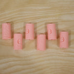 Six pink plastic bed sheet clips with a 'Love' design are arranged on a light wooden surface.