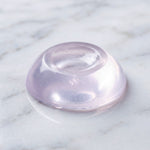 A single, clear, dome-shaped silicone door stopper with a slight purple hue rests on a white marble surface.