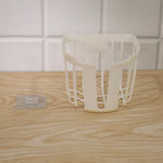 A white plastic toilet paper holder sits on a wooden surface next to a clear adhesive hook, with white tiles in the