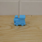A light blue plastic train-shaped pencil sharpener resting on a light brown wooden surface with a white tiled background.