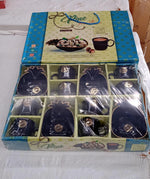 An open product box containing a black ceramic tea set with eight cups and four pineapple-shaped snack bowls, wrapped in