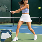 A woman in a white skort and lavender top plays tennis on a blue court, hitting a yellow ball.