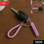 A pink braided wrist loop keychain with a car key and a pink number tag on a wooden table, with '1 Pc' and '20026' labels.