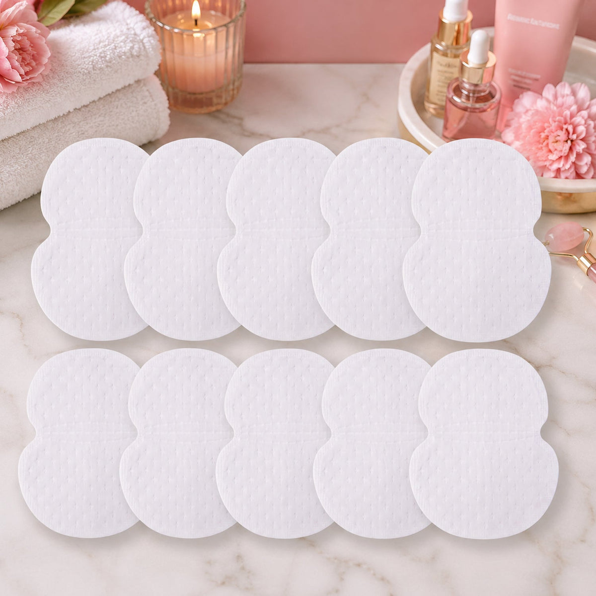 Ten white sweat pads are arranged on a marble surface with various beauty products and a lit candle in the background.