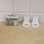 A product box and two white plastic bottle holders with their clear adhesive pads are arranged on a light wooden surface.