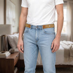 A man wearing light wash jeans and a white t-shirt, with two tan elastic belt hooks attached to his jeans, in a bedroom
