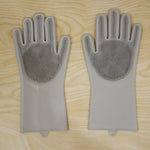 A pair of grey silicone scrubbing gloves with textured palms lays flat on a light wooden surface.