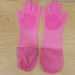 A pair of pink silicone scrubbing gloves with long, gathered cuffs laid flat on a light wooden surface.
