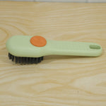 A green and orange liquid-dispensing brush with dark bristles is positioned on a light brown wooden surface.