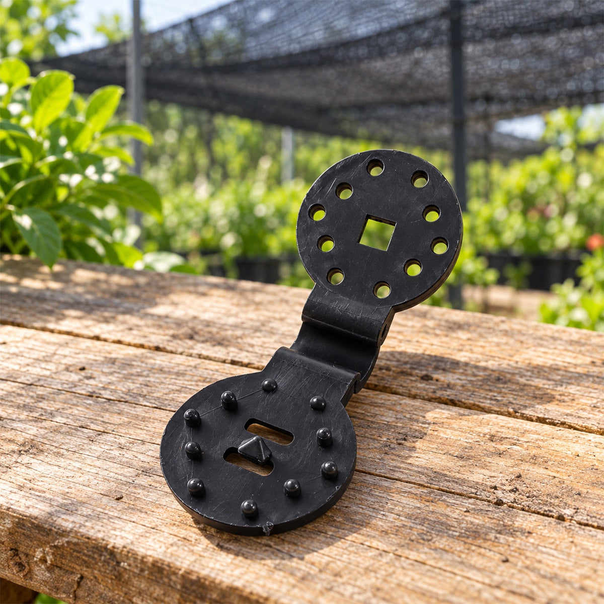 A single black plastic shade cloth clip with a hinged design, resting on a rustic wooden surface outdoors.