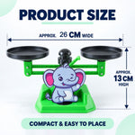A green elephant math balance scale with black pans, showing approximate dimensions of 26 cm wide and 13 cm high.