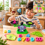 A smiling child places a pink number 3 on a green elephant math balance scale, surrounded by game pieces.